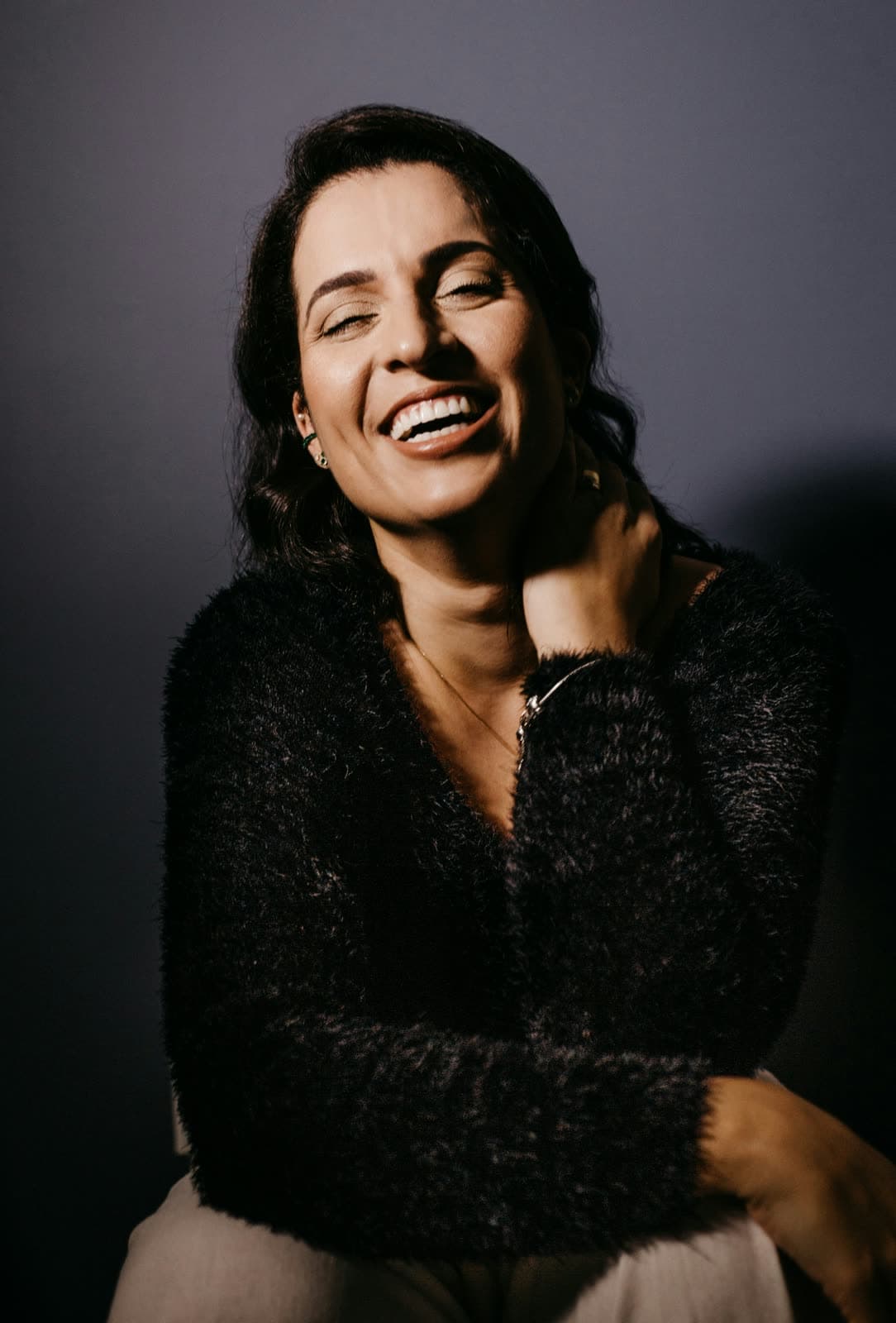 A woman laughing, wrapped in a soft black knit