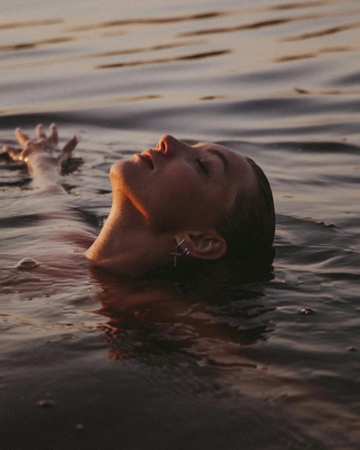 A woman floating on her back in open water at sunset, eyes closed